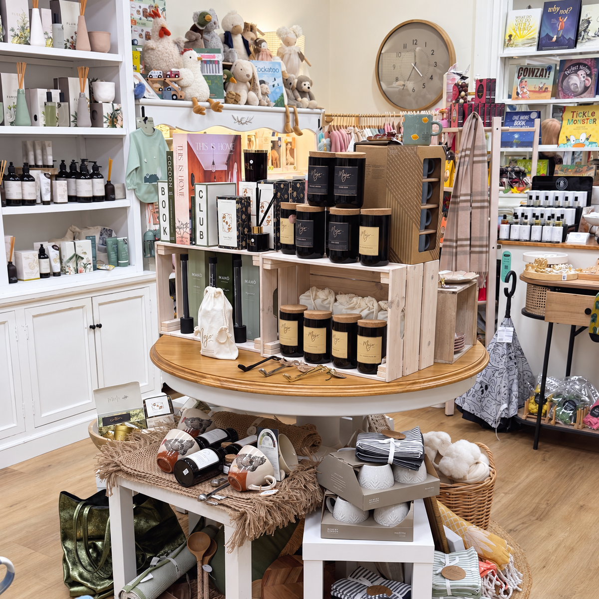 The round display at Purple Merchant, Mortdale: candles and diffusers on a timber table in front of white shelves of gifts