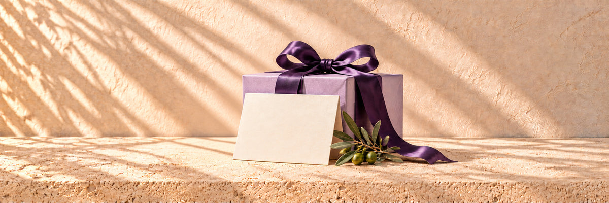 A blank ivory card against a lavender parcel, with purple satin and an olive sprig