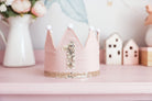 Pink first birthday crown on a shelf with flowers and little wooden houses