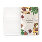 Open journal with lined pages beside an overhead grazing board and the words be joyful and happy together