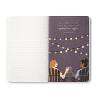 Open journal with lined pages beside an illustration of two people toasting under festoon lights