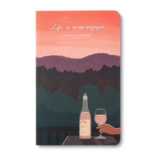 Journal cover of a coral sunset over layered hills with a hand raising a glass of wine