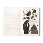 Open journal with lined pages beside a cream page of a silhouetted hand holding a flowering stem above a woven beehive, with bees