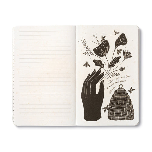 Open journal with lined pages beside a cream page of a silhouetted hand holding a flowering stem above a woven beehive, with bees