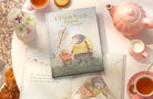 The book styled on a table with a pink teapot, cups and flowers