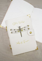 Dragonfly leather notebook lying on an open lined notebook on a linen cloth