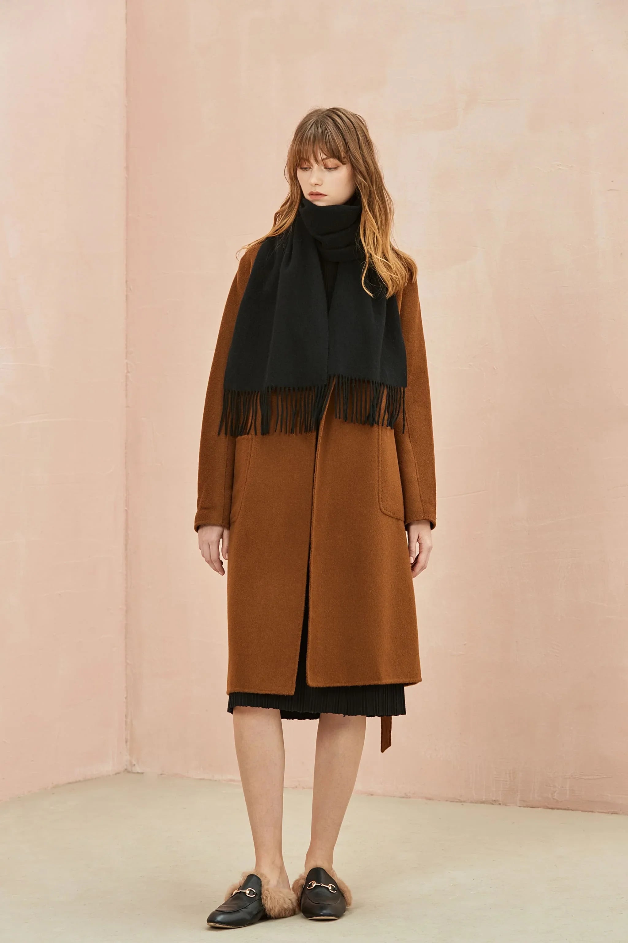 Full-length camel coat look with the Ebony black scarf, pink wall behind