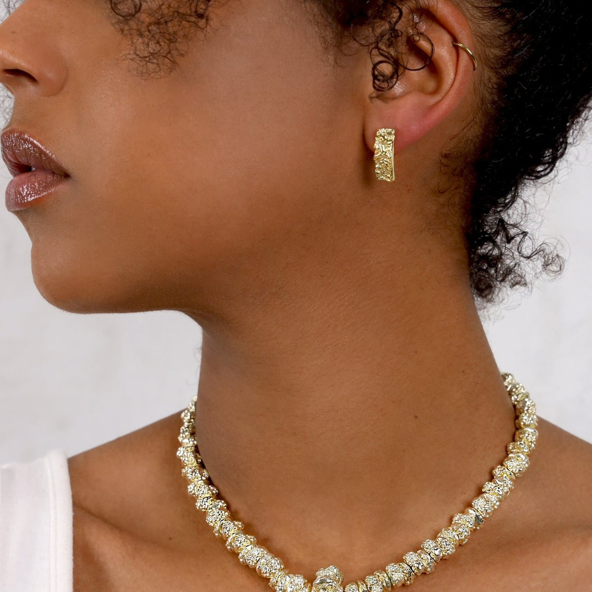 Bella gold earring worn by a model with a pale crystal necklace