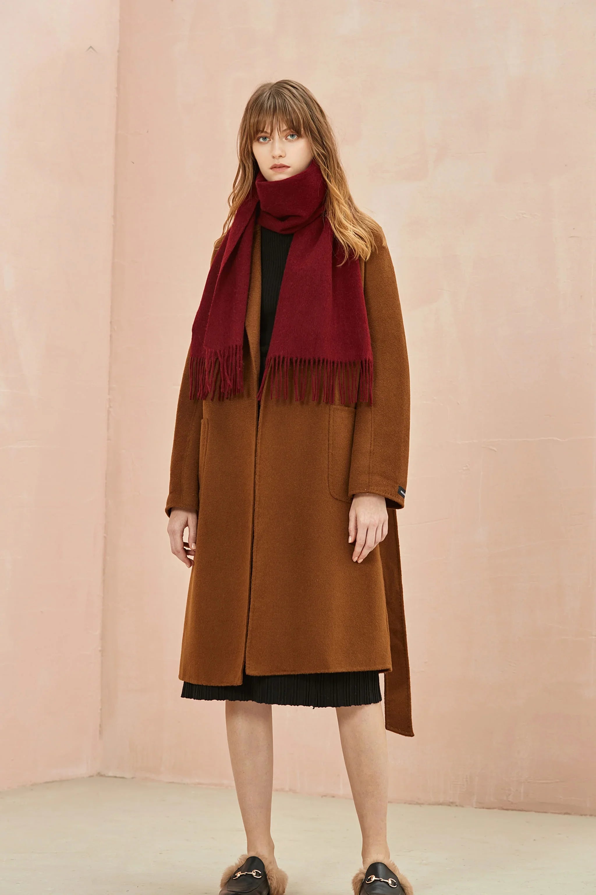 Full-length look with the Rhubarb burgundy scarf over a brown coat, pink wall behind