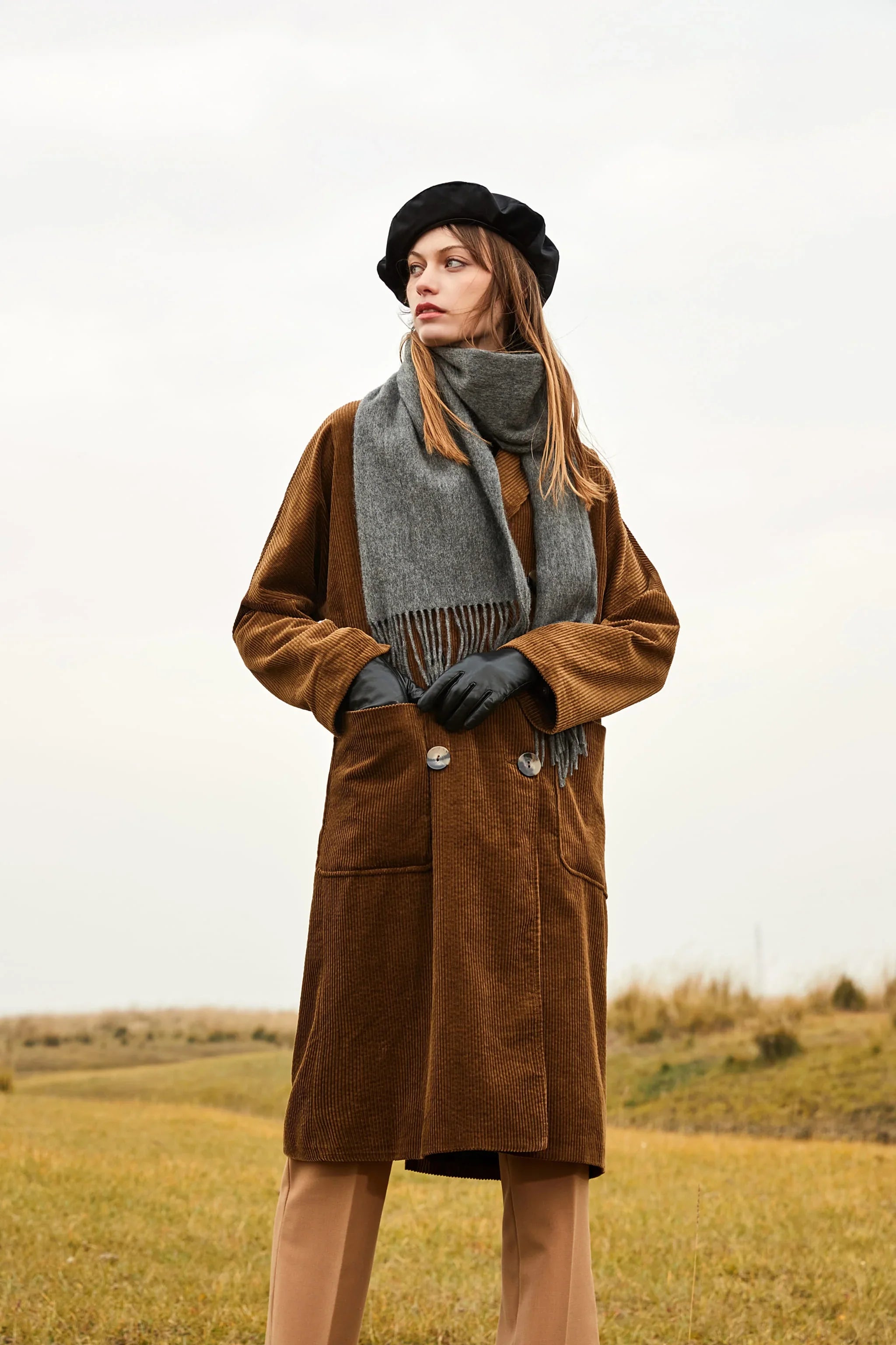 Model in a brown corduroy coat and beret wearing the Light Charcoal scarf in open country