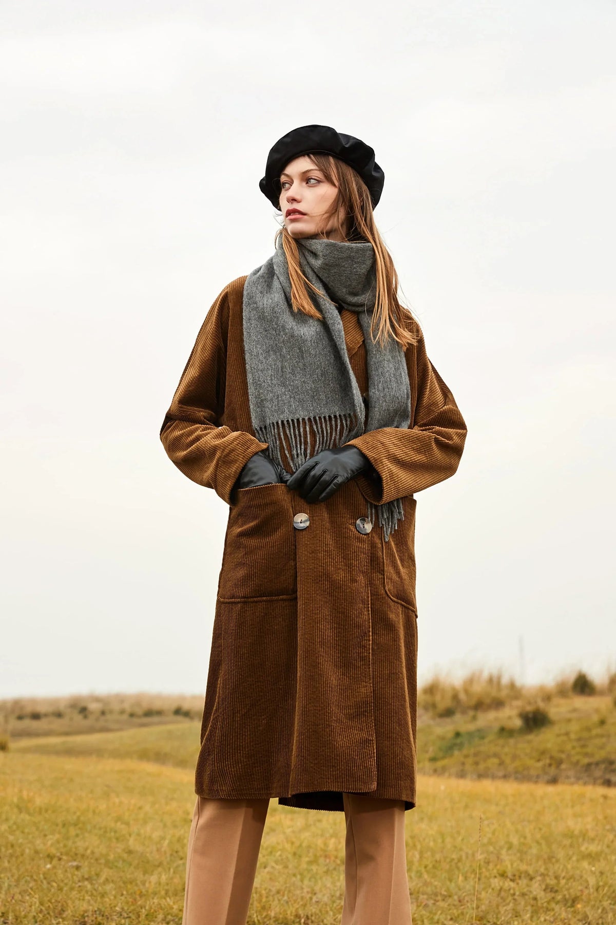 Model in a brown corduroy coat and beret wearing the Light Charcoal scarf in open country