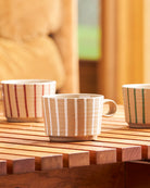 Three Archive mugs on a slatted timber table — chalk, sway and olive stripes