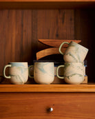 Four Jumble mugs in Azure stacked on a timber shelf with books