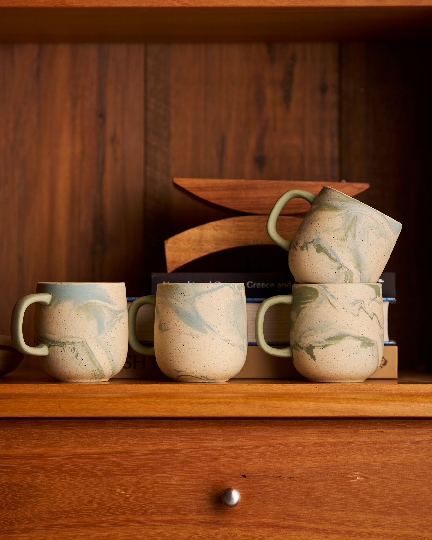 Four Jumble mugs in Azure stacked on a timber shelf with books