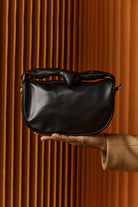 Hand holding the black Zala Bag against timber battens