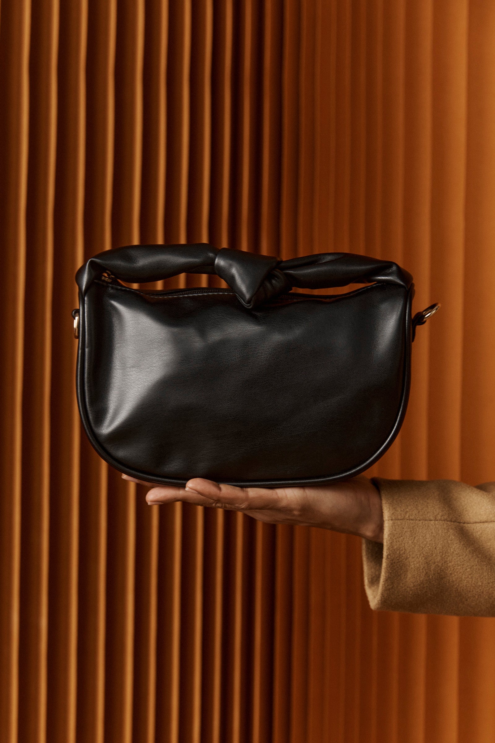 Hand holding the black Zala Bag against timber battens