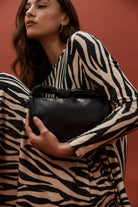 Model in zebra print holding the black Zala Bag