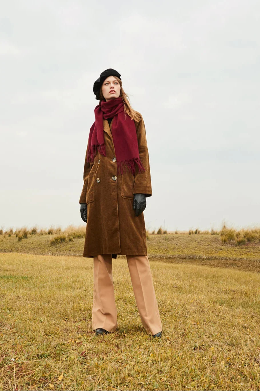 Model standing in a field wearing the Rhubarb burgundy scarf and beret