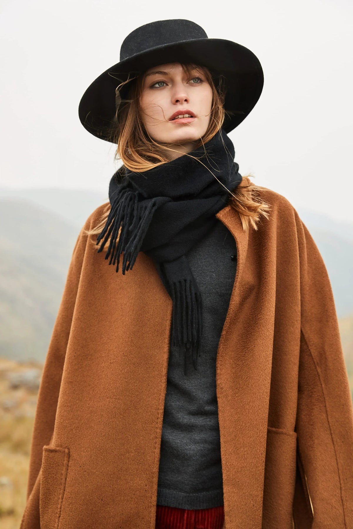 Model in a wide-brim black hat wearing the Ebony black merino scarf over a camel coat