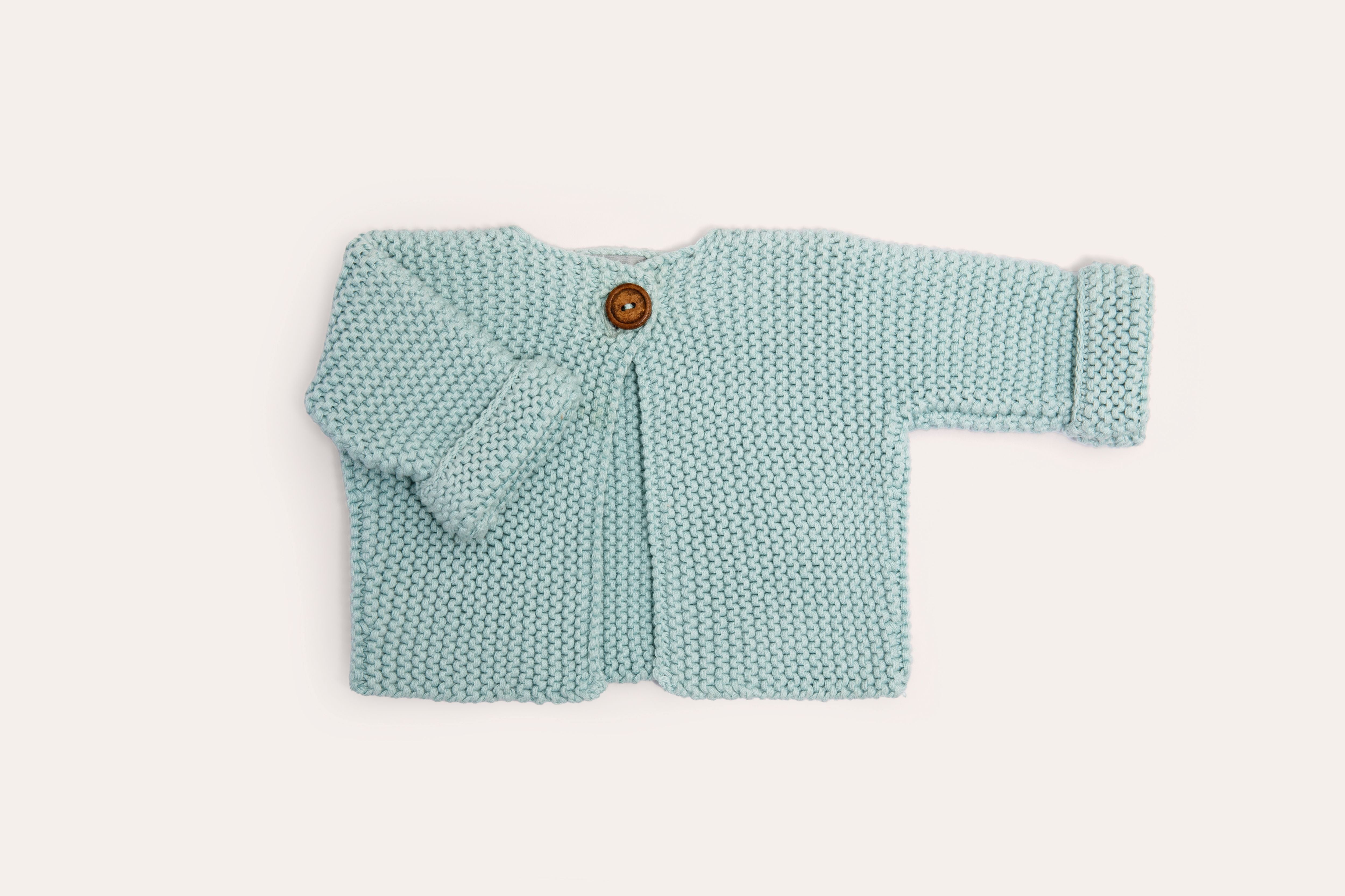 Baby Blue cardigan laid flat, fastened with a single wooden button, its cuffs turned back.