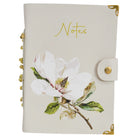 Cream leather notebook with a white magnolia print, Notes in gold script, a press-stud tab, gold-tone corners and gold beads on the spine