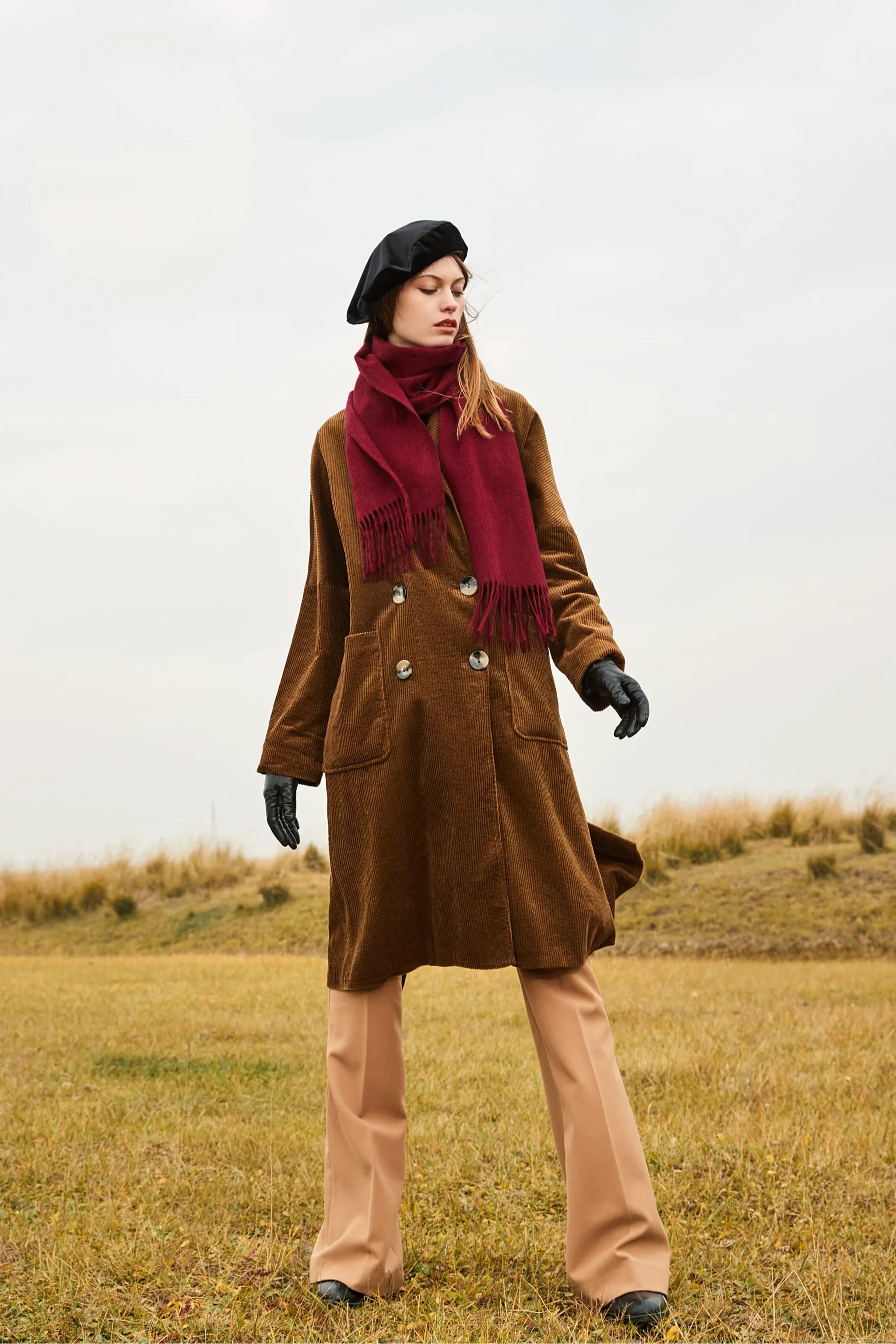 Model walking in grassland with the Rhubarb scarf and camel pants