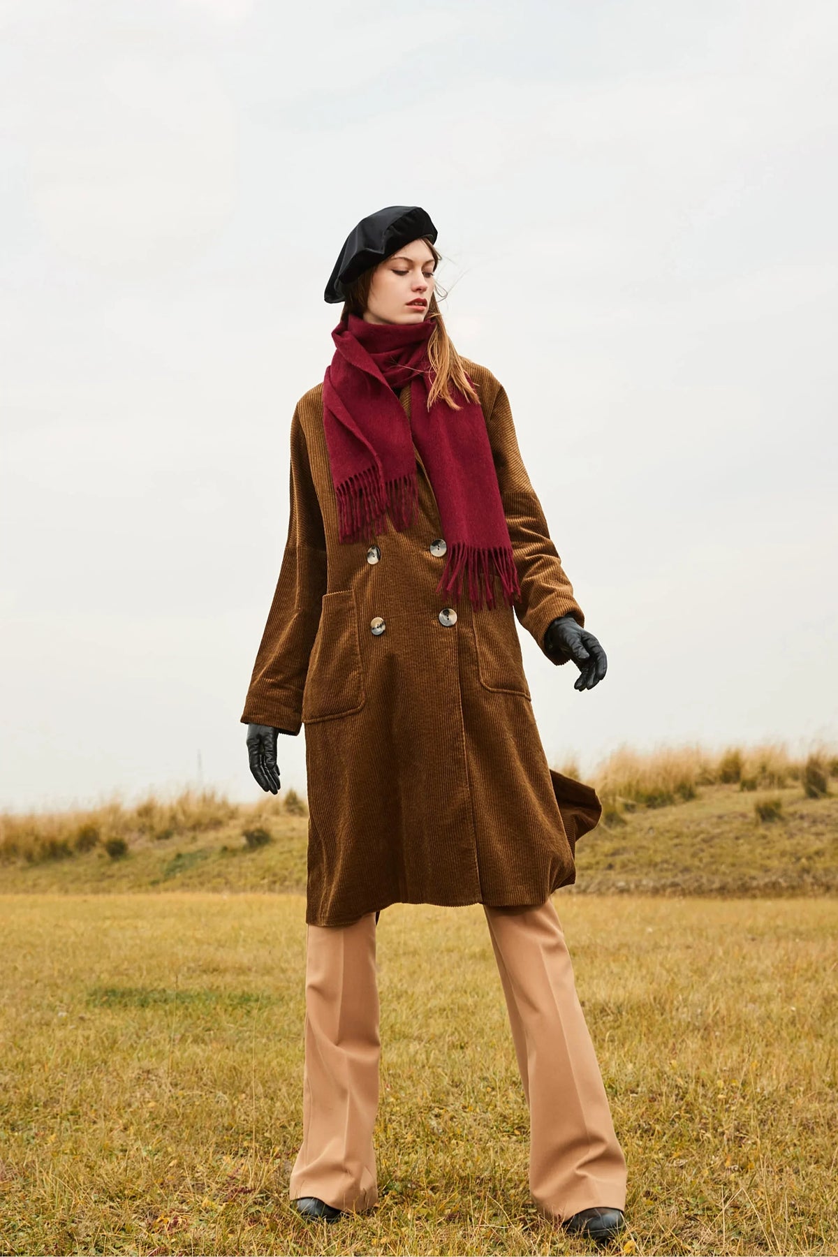 Model walking in grassland with the Rhubarb scarf and camel pants