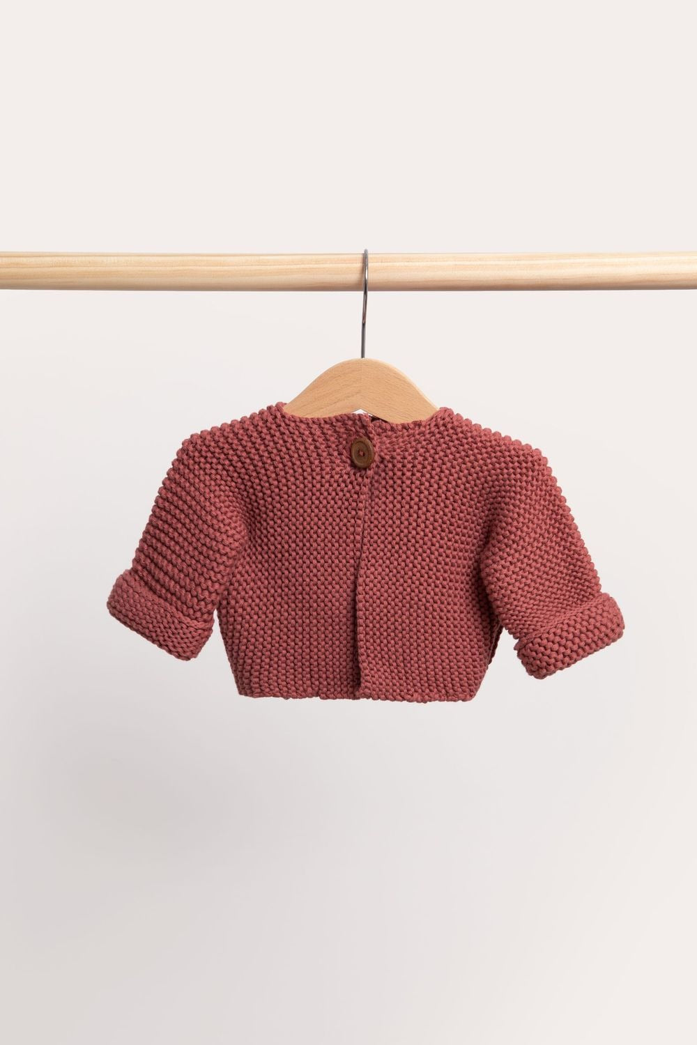 Dusty cardigan in a muted rose red, on a wooden hanger from a timber rail.