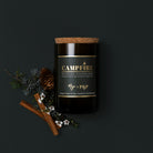 Campfire candle in a dark reclaimed bottle on charcoal, with pine sprig, pinecones and cinnamon sticks