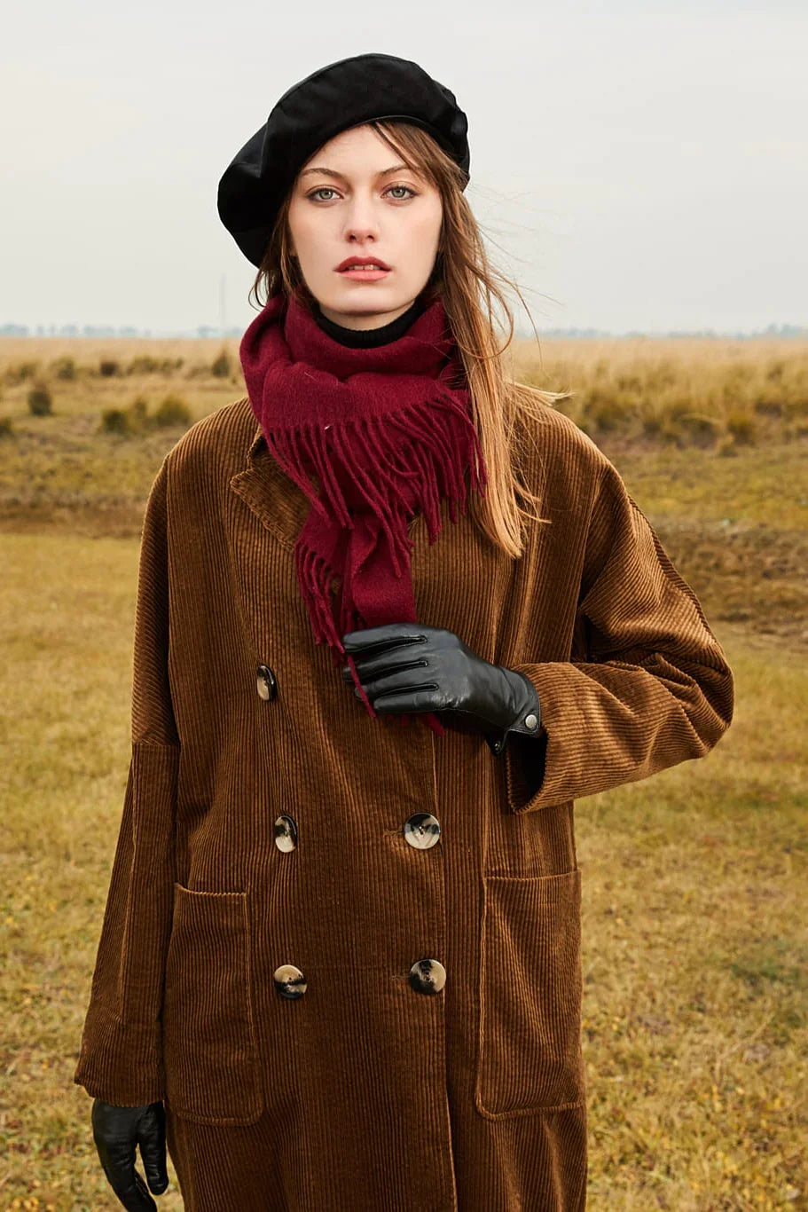 Rhubarb burgundy scarf wrapped at the neck of a brown coat in open country