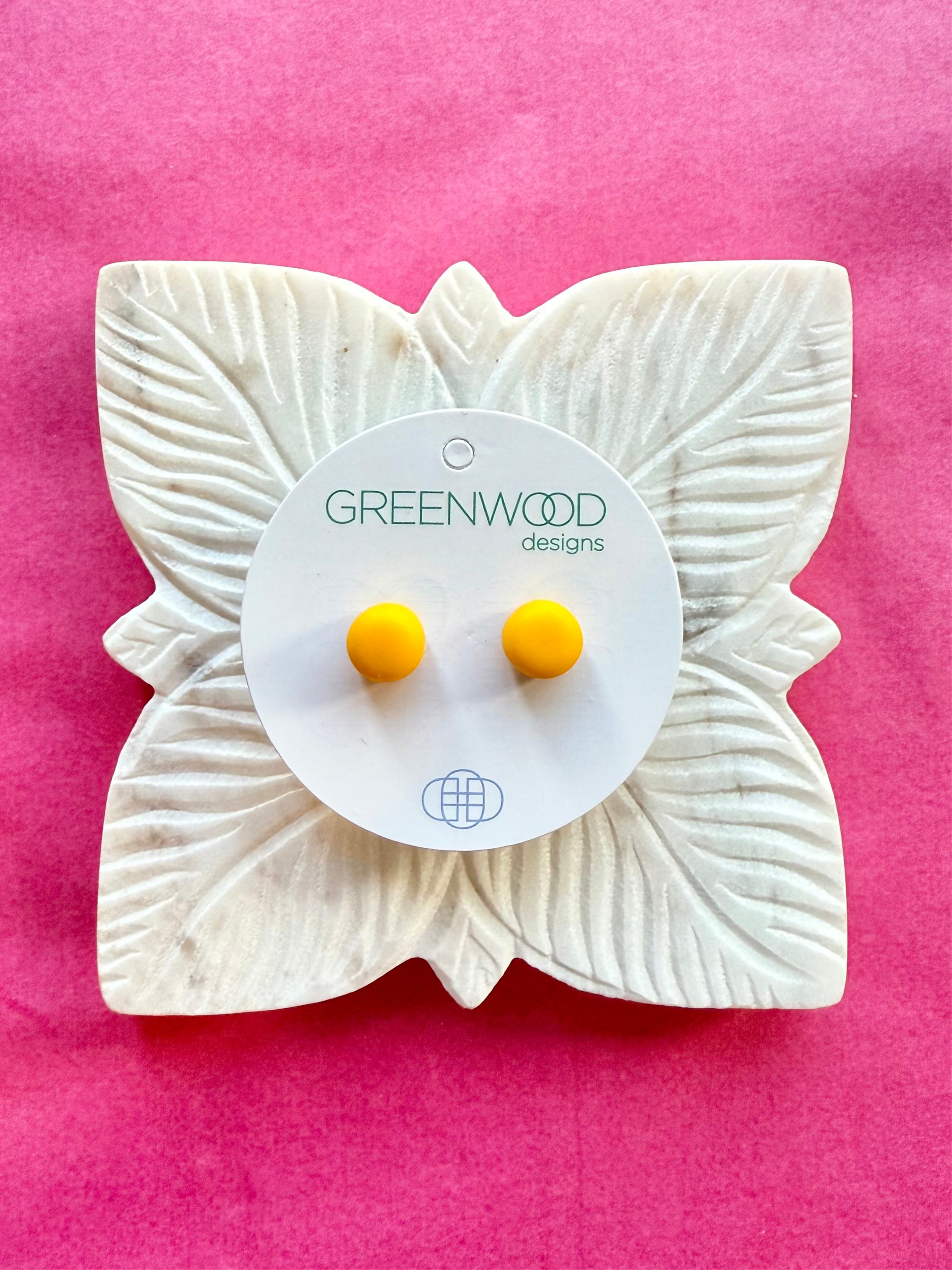 Round earrings in Yellow: a pair of sunflower-yellow resin studs on a round card, on a carved white leaf dish against pink paper.