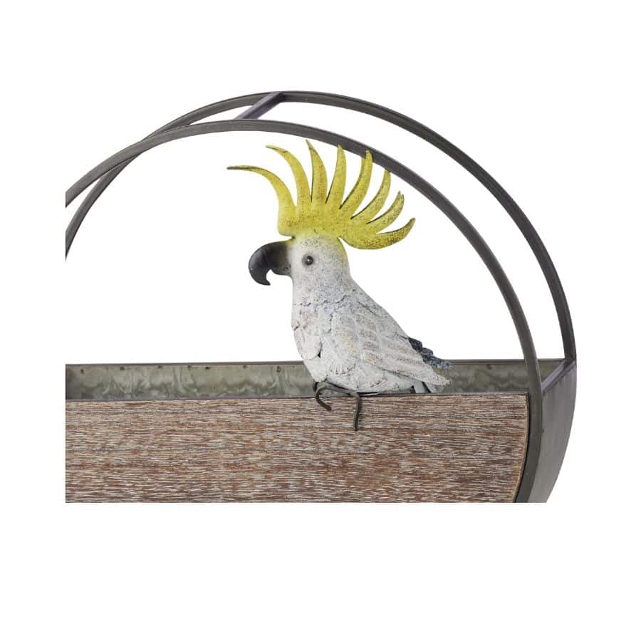 White sulphur-crested cockatoo with a bright yellow crest, perched on a curved dark metal arc that hooks over the edge of a pot.