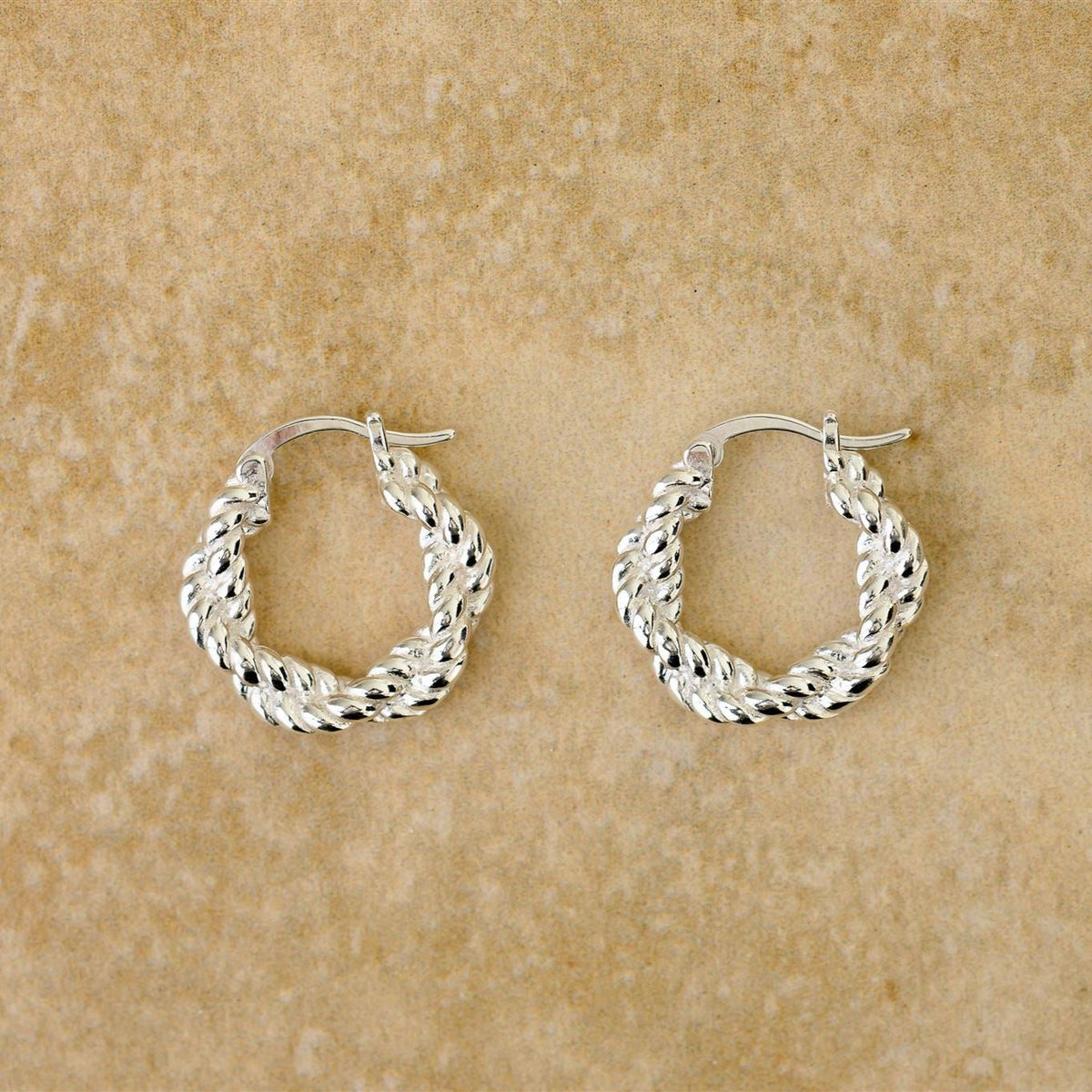 Pair of Stevie twisted sterling silver hoop earrings on a sandstone surface