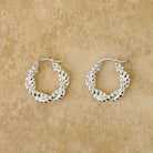 Pair of Stevie twisted sterling silver hoop earrings on a sandstone surface