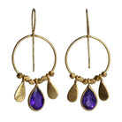 Fine gold hoop earrings with a faceted violet amethyst teardrop between two gold petals