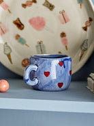 Blue cup with red hearts on a shelf in front of a painted plate