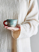 Blue cloud cup held in an open hand against a cream knit sleeve