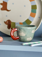 Blue cloud cup on a shelf in front of a painted plate