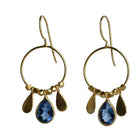 Fine gold hoop earrings with a faceted deep blue London blue topaz teardrop between two gold petals