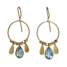 Fine gold hoop earrings with a faceted pale sky-blue topaz teardrop between two gold petals