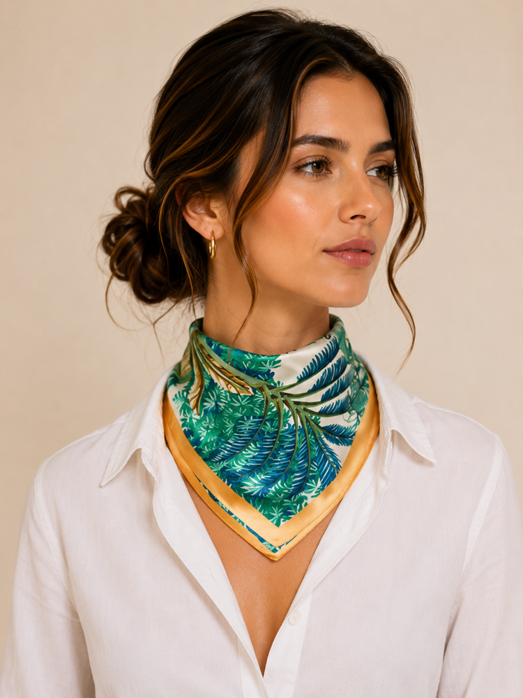 Model in a white shirt wearing a green and blue fern-print silk scarf with a golden satin border knotted at the neck