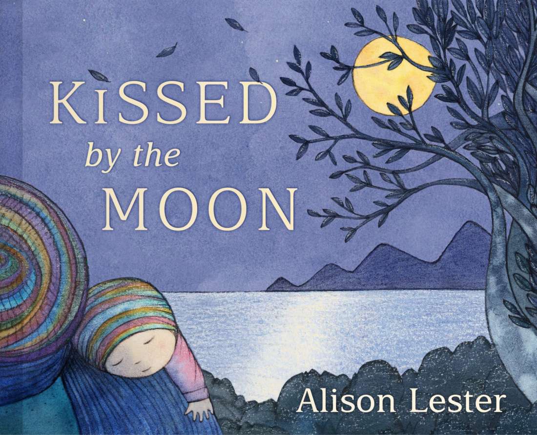 Kissed by the Moon by Alison Lester, a blue cover of a baby in a striped beanie asleep against a rainbow-striped figure, with the sea, hills, a tree and a full moon