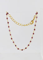 Fine gold chain bracelet with faceted garnet-red beads draped on a stand