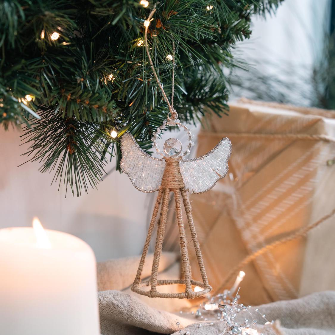 Angel ornament with a jute-wrapped wire body, clear beaded wings edged in silver wire and a faceted bead head, hanging from a Christmas tree beside a lit pillar candle