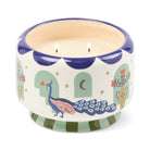 Wide cream ceramic candle with a navy scalloped rim, painted with a peacock and mint arches, its two wicks lit.
