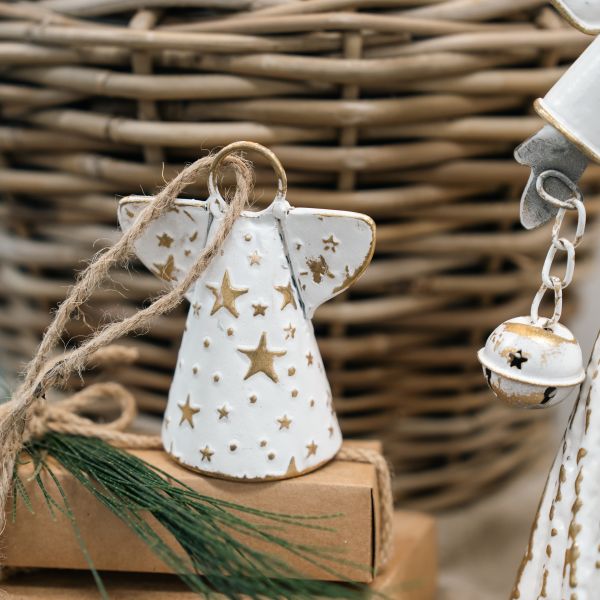 White metal angel with embossed gold stars and gold-edged wings standing on a kraft box, a jute loop through her ring, a white and gold jingle bell on a chain at the right edge