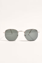 Metal frame hexagonal sunglasses with dark green-grey lenses, front view on a cream background