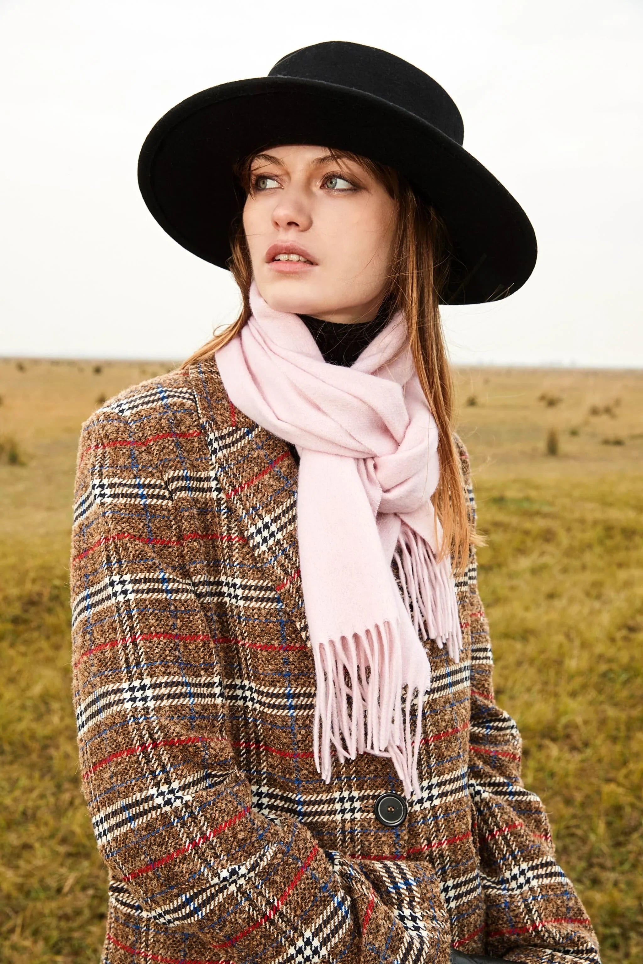 Model in a black hat and houndstooth coat wearing the Dahlia pink merino scarf outdoors