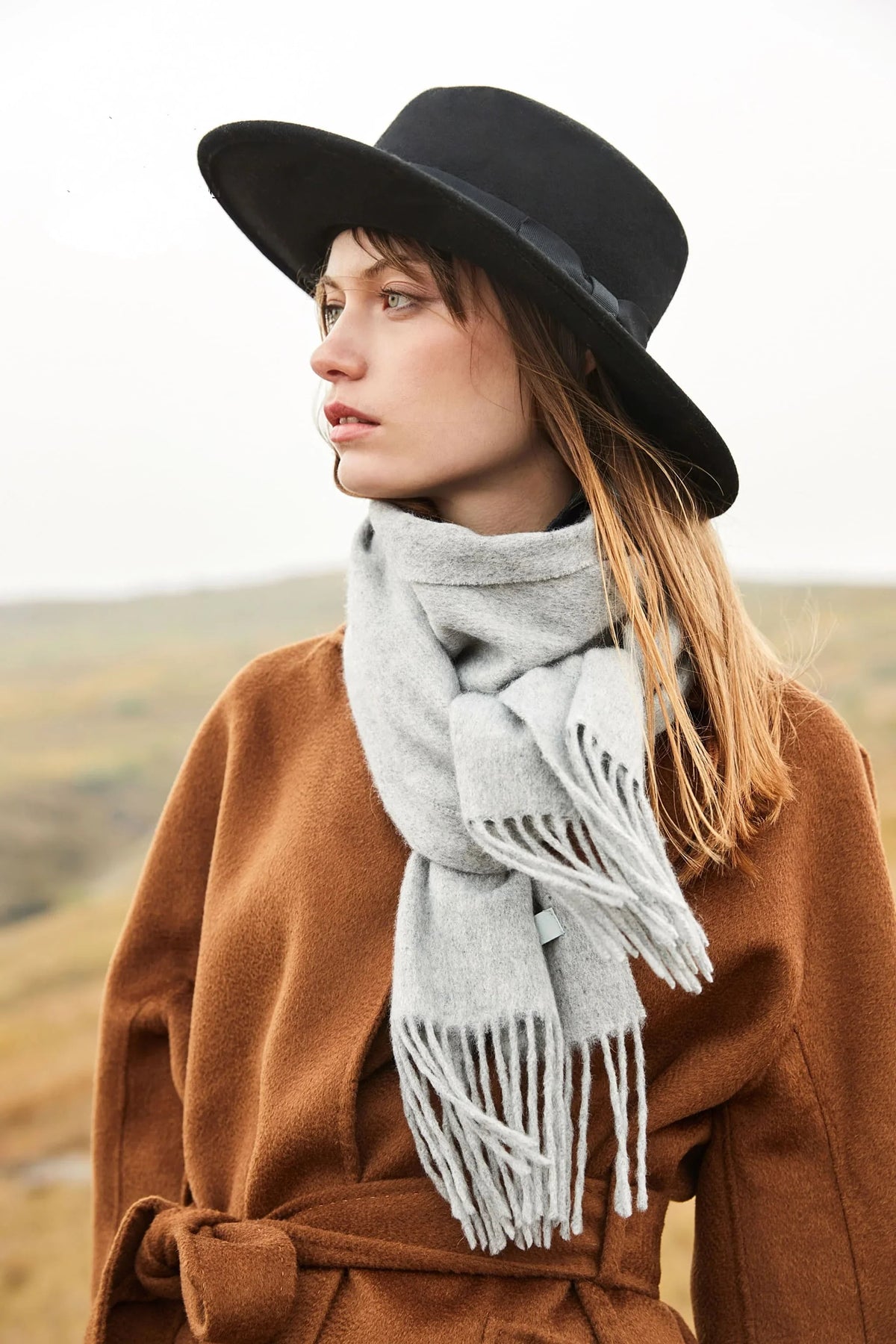 Model in a black hat and brown wrap coat wearing the Quartz light grey scarf outdoors