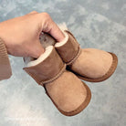 Hands holding a pair of chestnut sheepskin baby booties showing the cream wool lining